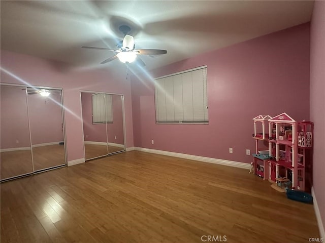 unfurnished bedroom featuring two closets, ceiling fan, and hardwood / wood-style floors