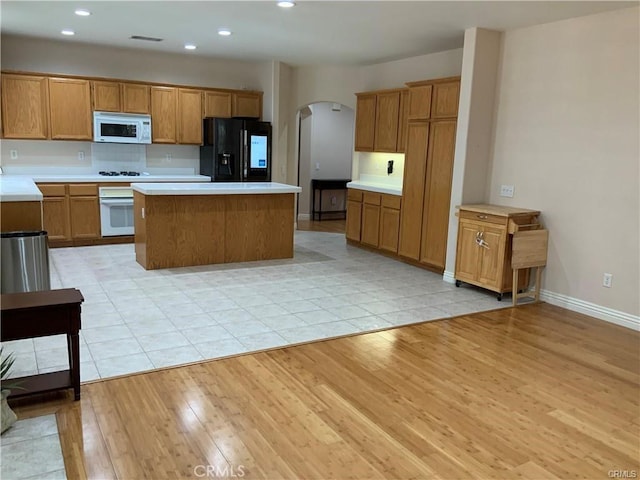 kitchen with white appliances, light wood-type flooring, backsplash, and a kitchen island