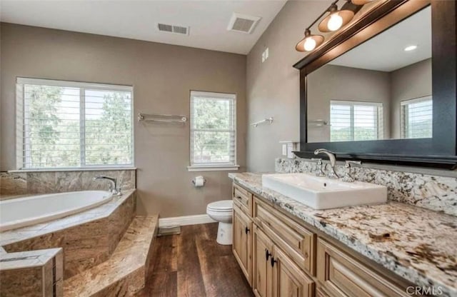 bathroom featuring hardwood / wood-style flooring, tiled tub, vanity, and toilet