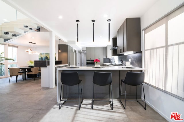 kitchen featuring gray cabinets, a breakfast bar, decorative backsplash, kitchen peninsula, and wall chimney range hood