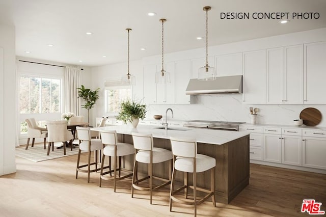 kitchen with light hardwood / wood-style floors, a center island with sink, tasteful backsplash, decorative light fixtures, and white cabinets