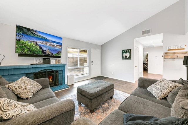 living room with a tile fireplace, vaulted ceiling, and wood-type flooring