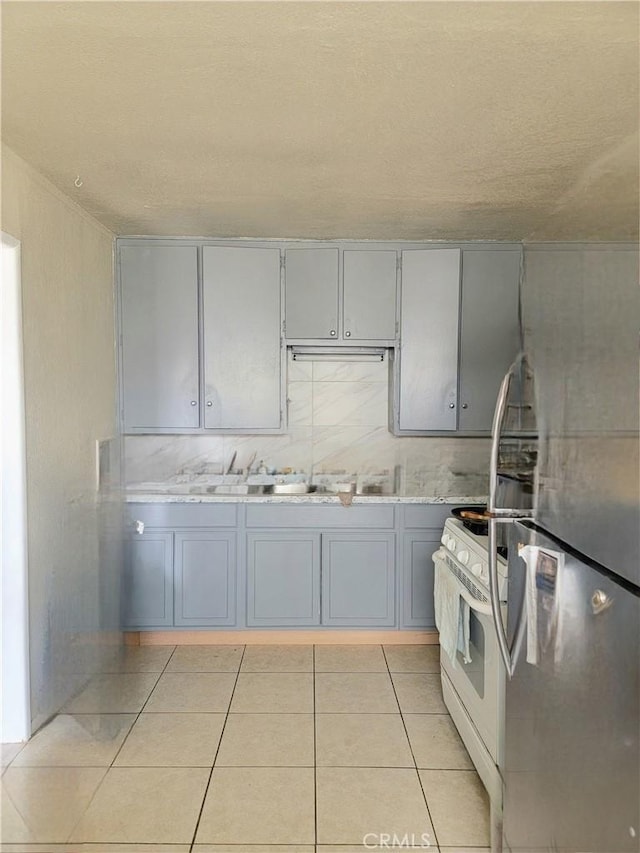 kitchen featuring white range with gas cooktop, light tile patterned floors, light stone countertops, gray cabinetry, and stainless steel fridge