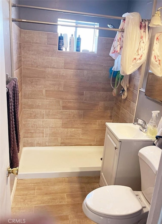 bathroom featuring wood-type flooring, tiled shower, vanity, and toilet