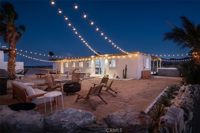 patio at night with an outdoor fire pit and a hot tub