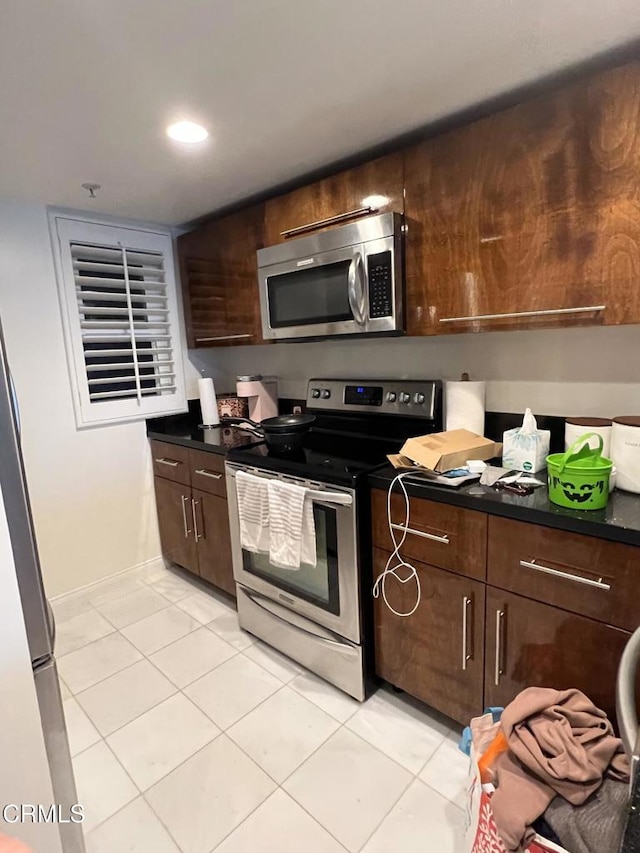 kitchen featuring appliances with stainless steel finishes, light tile patterned flooring, and dark brown cabinetry