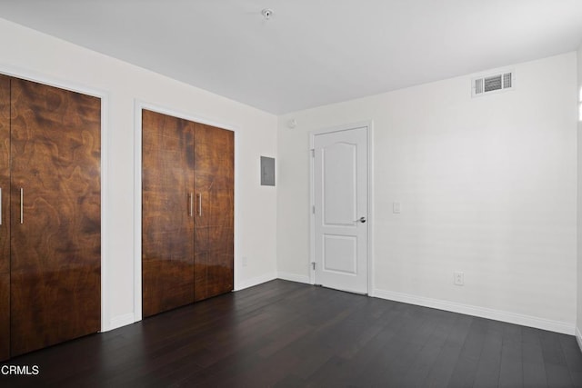 unfurnished bedroom featuring dark wood-style floors, baseboards, electric panel, and visible vents