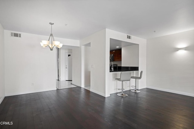 unfurnished living room featuring visible vents, an inviting chandelier, and wood finished floors