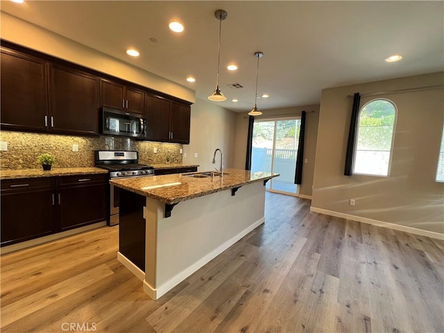 kitchen featuring sink, a kitchen island with sink, a breakfast bar area, stainless steel appliances, and light stone counters