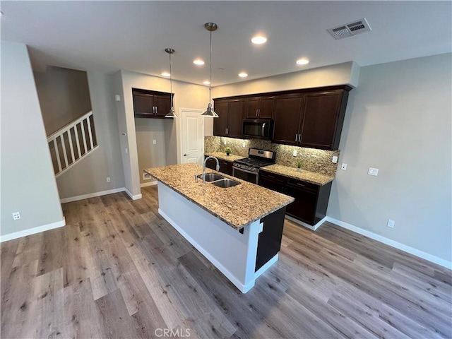 kitchen with a center island with sink, appliances with stainless steel finishes, pendant lighting, light stone counters, and sink