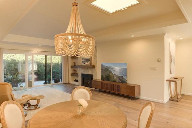 dining area with a chandelier, a large fireplace, a raised ceiling, and light hardwood / wood-style floors