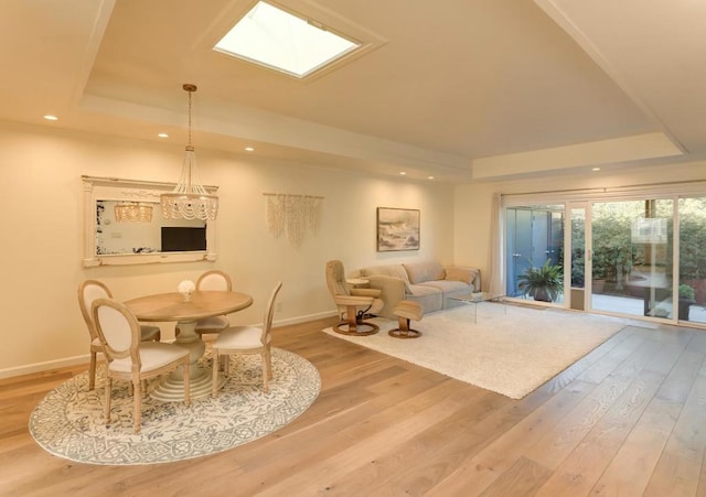 dining area with a skylight, a raised ceiling, and light hardwood / wood-style floors