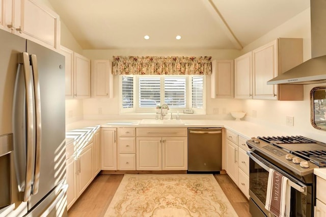 kitchen with vaulted ceiling, appliances with stainless steel finishes, sink, wall chimney exhaust hood, and light hardwood / wood-style flooring