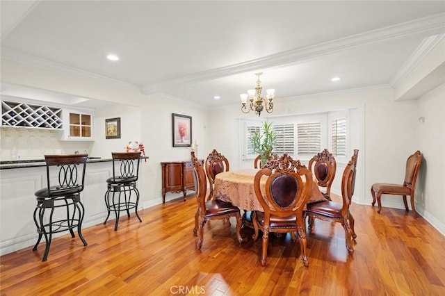 dining space with indoor bar, an inviting chandelier, ornamental molding, and light hardwood / wood-style flooring