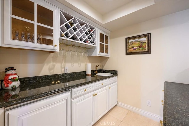 kitchen featuring sink, white cabinets, light tile patterned floors, and dark stone counters