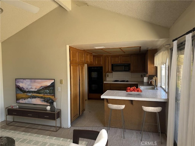 kitchen with vaulted ceiling, tile countertops, kitchen peninsula, backsplash, and black appliances