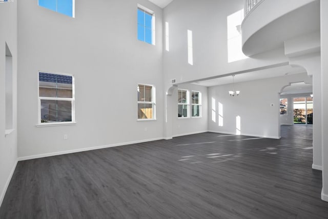 unfurnished living room with a towering ceiling, a notable chandelier, and dark wood-type flooring