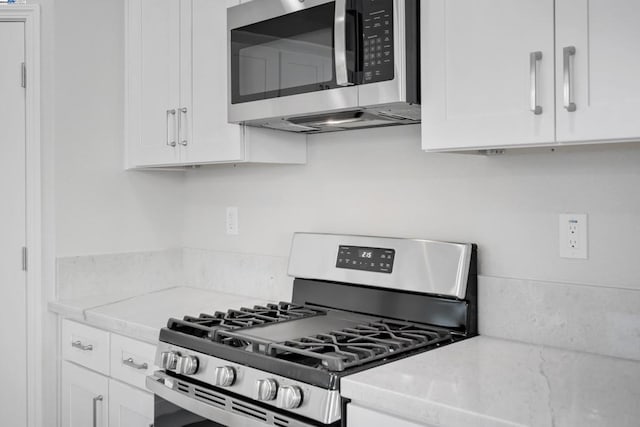 kitchen with light stone counters, appliances with stainless steel finishes, and white cabinetry