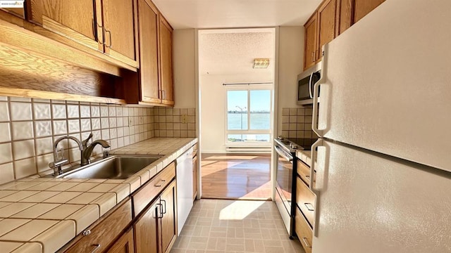 kitchen with appliances with stainless steel finishes, a water view, tile countertops, decorative backsplash, and sink