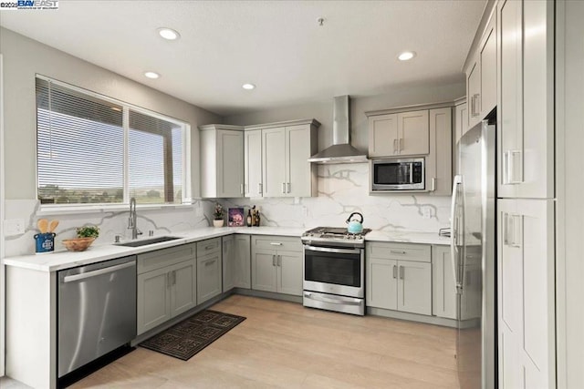 kitchen featuring light hardwood / wood-style flooring, wall chimney range hood, tasteful backsplash, appliances with stainless steel finishes, and sink