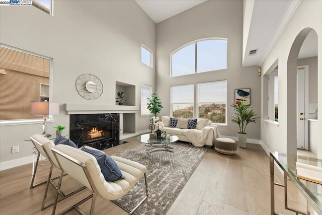 living room with a towering ceiling, light wood-type flooring, a premium fireplace, built in shelves, and crown molding