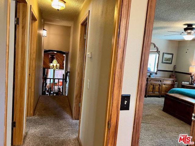 hall with a textured ceiling, an inviting chandelier, and carpet floors