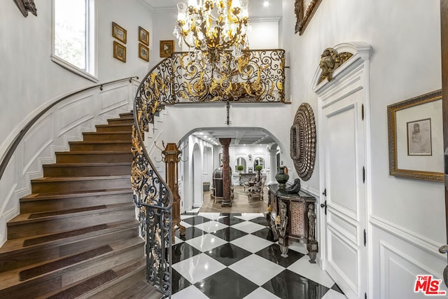 foyer with a towering ceiling, crown molding, a chandelier, and ornate columns