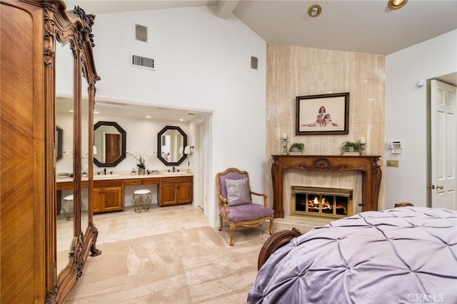 bedroom featuring a high end fireplace, light colored carpet, beamed ceiling, sink, and ensuite bathroom