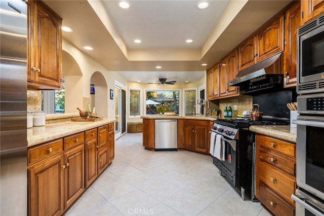 kitchen featuring kitchen peninsula, light stone countertops, a raised ceiling, backsplash, and appliances with stainless steel finishes