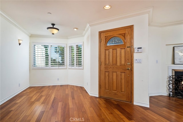 entryway with dark wood-type flooring, crown molding, and a fireplace