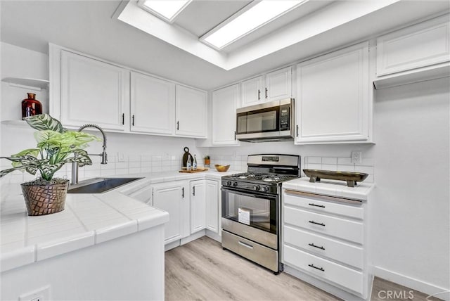 kitchen with tile countertops, light hardwood / wood-style flooring, white cabinetry, appliances with stainless steel finishes, and sink