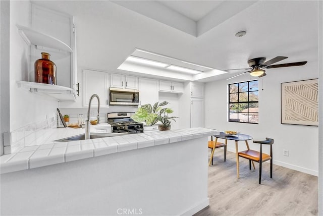 kitchen with sink, white cabinets, kitchen peninsula, tile counters, and appliances with stainless steel finishes