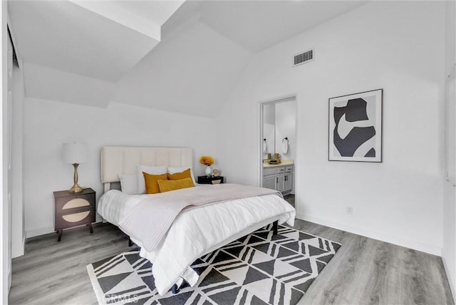 bedroom with lofted ceiling, light hardwood / wood-style floors, and connected bathroom