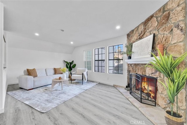 living room with vaulted ceiling, light hardwood / wood-style flooring, and a stone fireplace