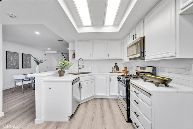 kitchen with sink, white cabinetry, light hardwood / wood-style flooring, kitchen peninsula, and appliances with stainless steel finishes