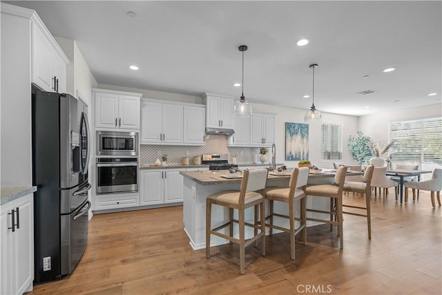 kitchen with appliances with stainless steel finishes, a kitchen island with sink, white cabinetry, and light stone countertops