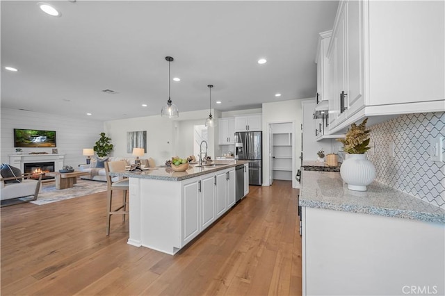 kitchen with light stone countertops, an island with sink, white cabinetry, and pendant lighting