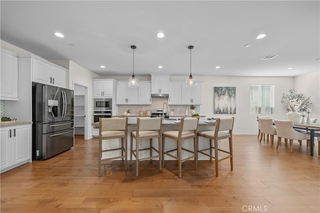 kitchen featuring an island with sink, stainless steel appliances, tasteful backsplash, decorative light fixtures, and white cabinets