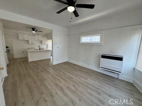 unfurnished living room featuring light hardwood / wood-style floors, ceiling fan, heating unit, and sink