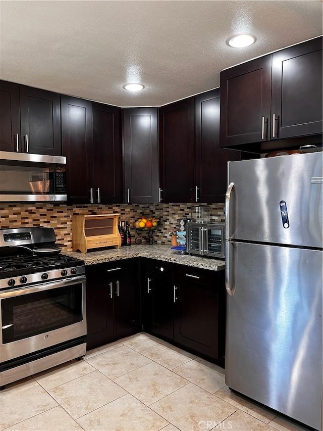 kitchen with light stone countertops, appliances with stainless steel finishes, a textured ceiling, and dark brown cabinets