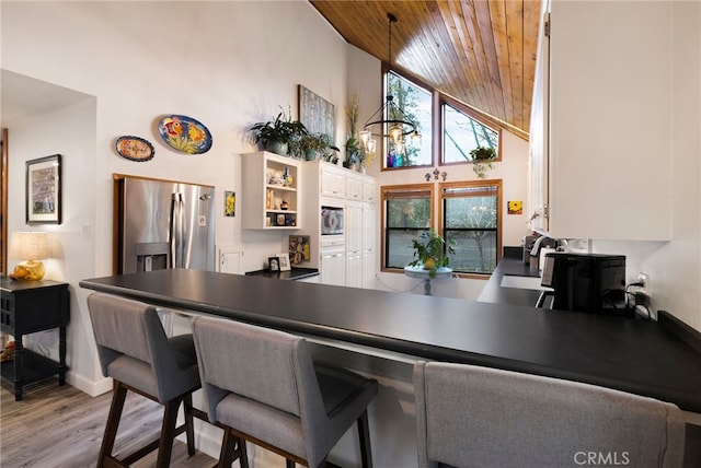 kitchen with white cabinets, light wood-type flooring, a high ceiling, wood ceiling, and appliances with stainless steel finishes