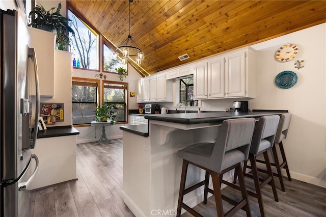 kitchen with white cabinetry, kitchen peninsula, stainless steel refrigerator, high vaulted ceiling, and pendant lighting