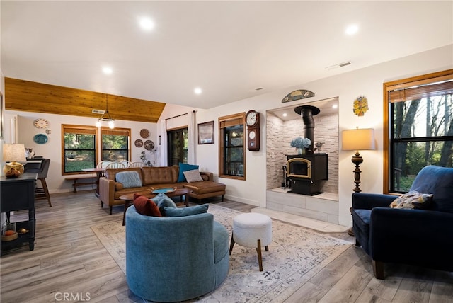 living room with light hardwood / wood-style floors, vaulted ceiling with beams, and a wood stove