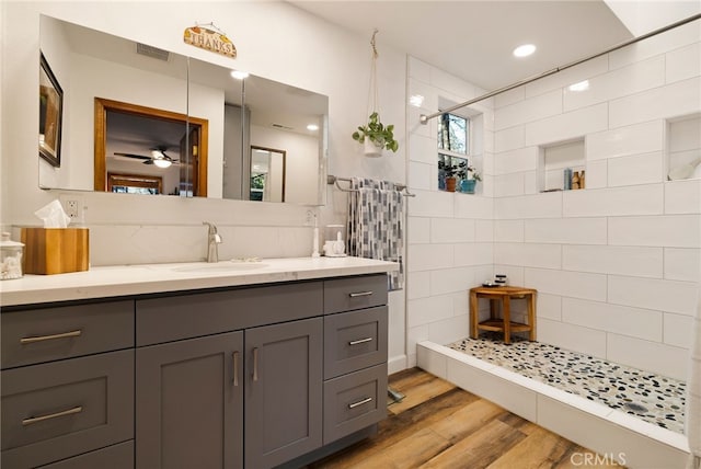 bathroom with ceiling fan, hardwood / wood-style flooring, a tile shower, backsplash, and vanity