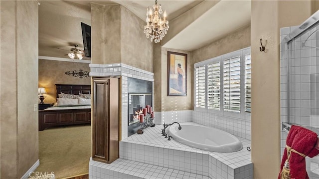 bathroom with tiled tub and ceiling fan with notable chandelier