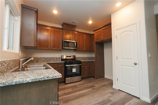 kitchen featuring light stone counters, sink, light hardwood / wood-style floors, and appliances with stainless steel finishes