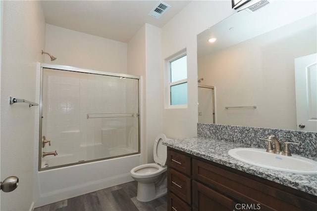 full bathroom featuring bath / shower combo with glass door, hardwood / wood-style floors, vanity, and toilet