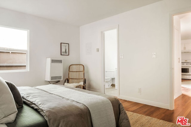 bedroom with ensuite bathroom, light hardwood / wood-style floors, and heating unit