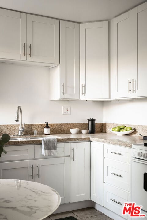 kitchen featuring white cabinets, tile patterned flooring, white gas range, and sink