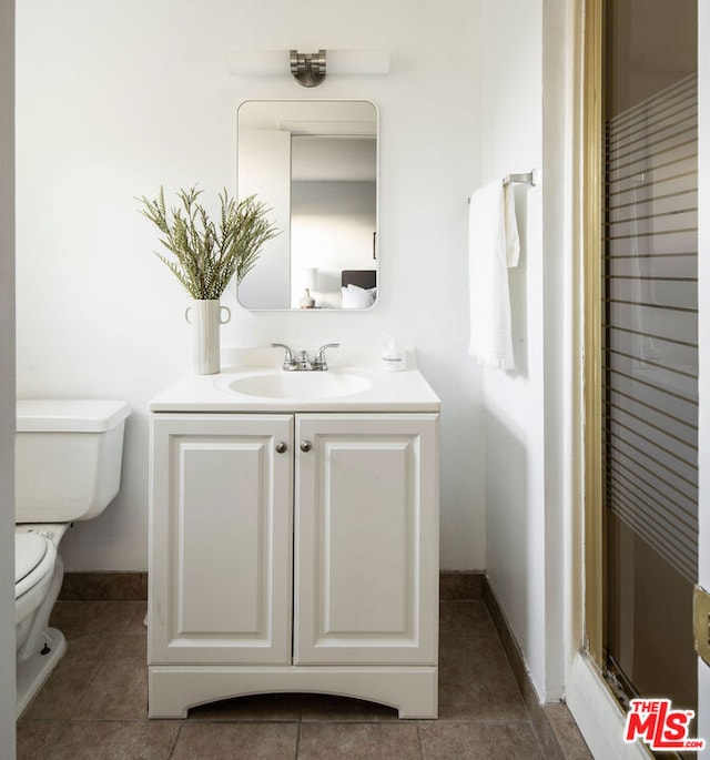 bathroom with toilet, tile patterned flooring, a shower with door, and vanity